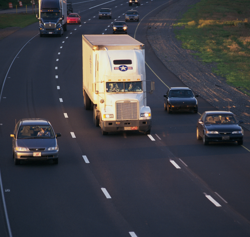 En la imagen se muestra un camión con vehículos en la carretera