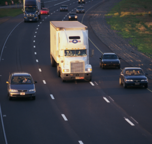 En la imagen se muestra un camión con vehículos en la carretera